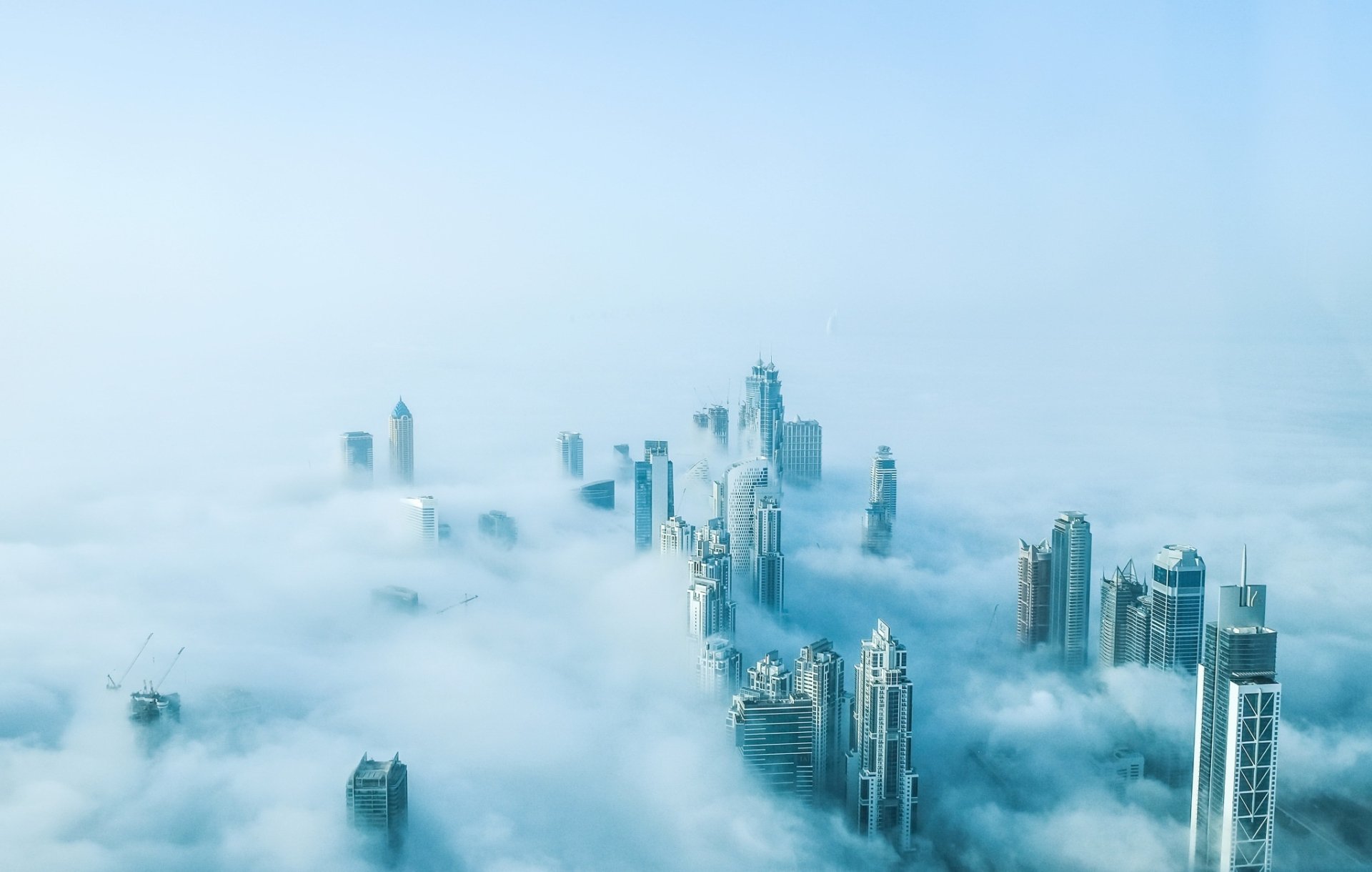 Aerial view of Dubai's skyscrapers emerging through dense fog, captured in high-definition. The image showcases the city's impressive architecture set against a misty backdrop.