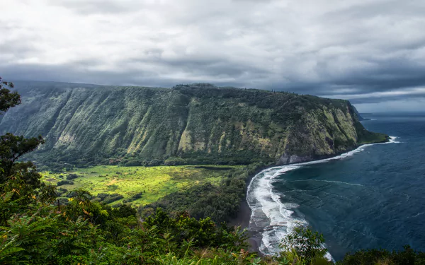 4K Ultra HD view of a dramatic Hawaiian coastline with rugged cliffs, lush greenery, and ocean waves under a cloudy sky, showcasing nature's beauty.