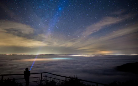 A person shines a blue laser into a starry night sky, creating a Sci-Fi ambiance. The panoramic HD wallpaper captures the horizon and the vast expanse of stars above.
