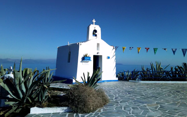 A small white church with a cross on top set against a clear blue sky and ocean, captured in stunning 4K Ultra HD as a religious PC desktop wallpaper.