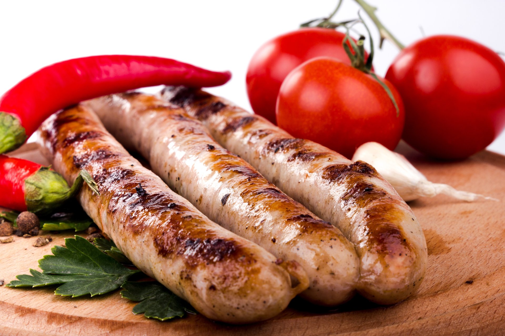 Close-up of grilled sausages with fresh red peppers and tomatoes on a wooden board, captured in stunning 4K Ultra HD for a vibrant food wallpaper.