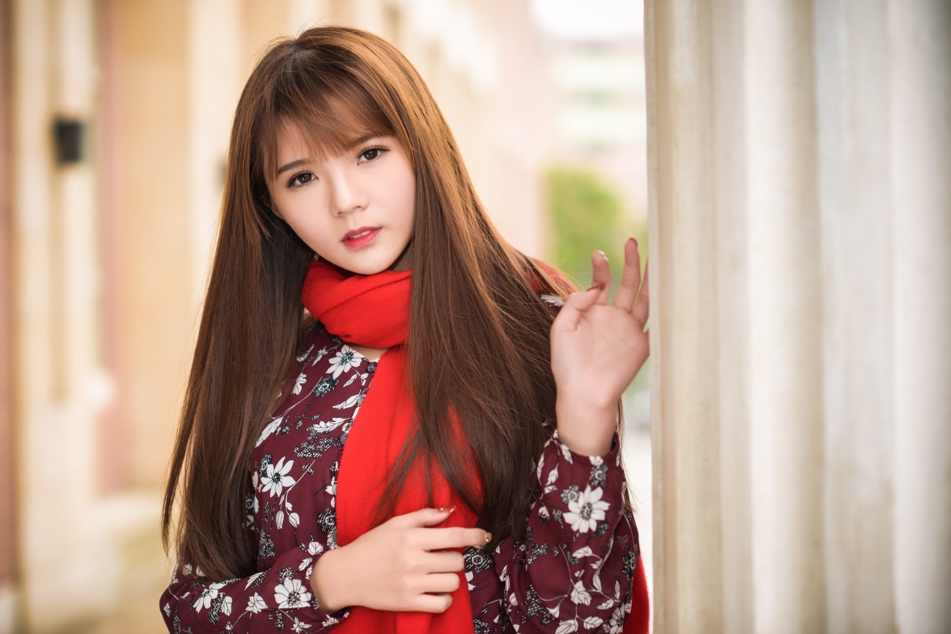 HD wallpaper featuring an Asian brunette model with brown eyes wearing a floral top and red scarf, posing gracefully against a light-colored backdrop.