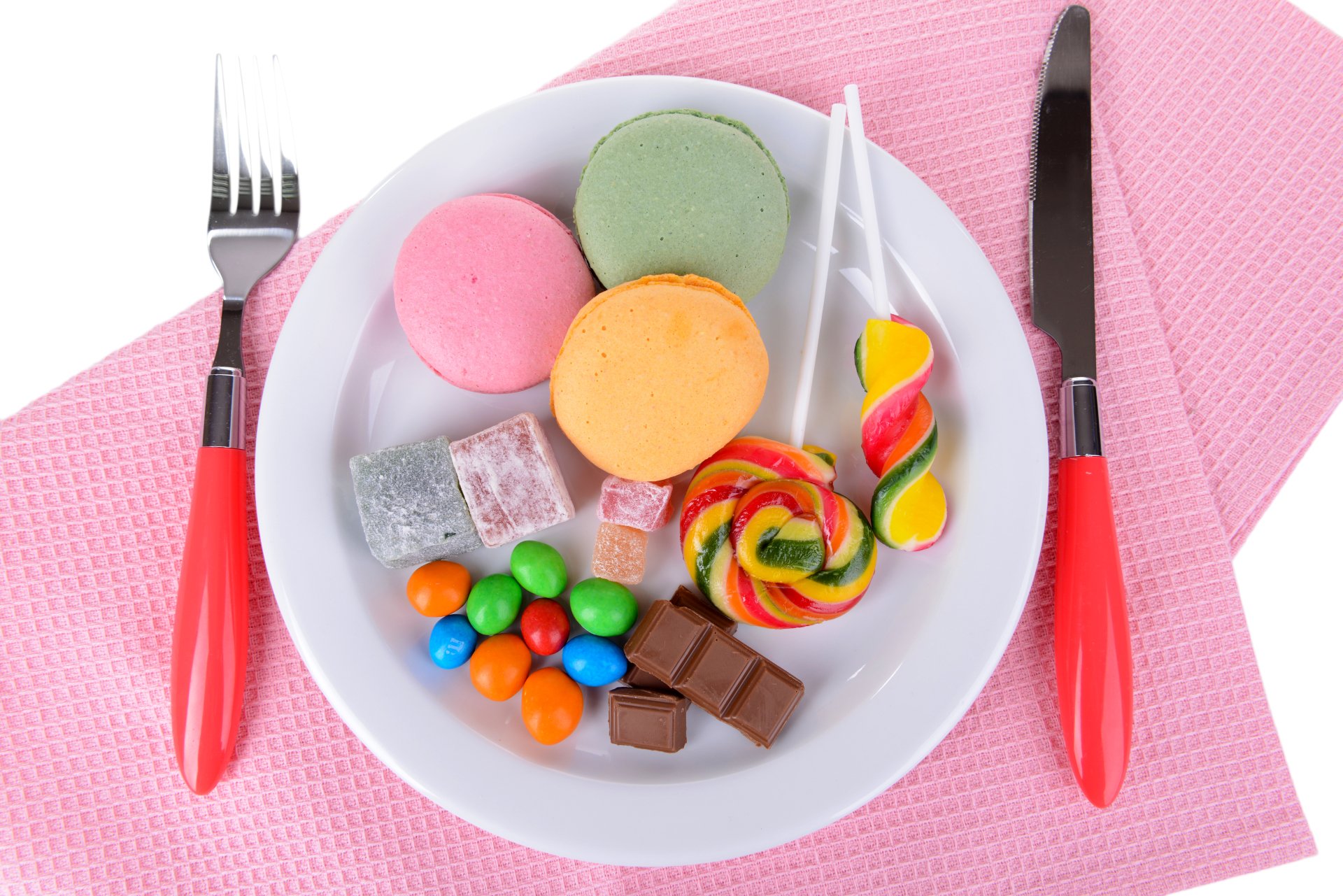 Colorful macarons, lollipop, chocolate pieces, and candy arranged on a white plate with red-handled fork and knife on a pink textured background, in 4K Ultra HD.