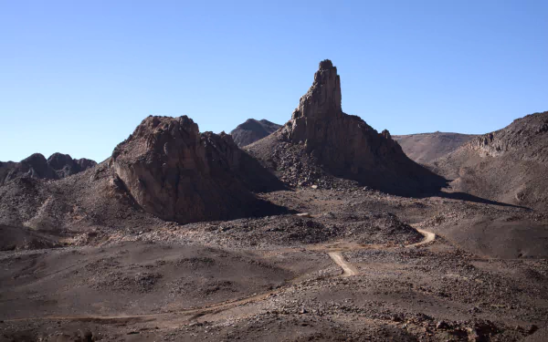 Sunny Sahara scene at Assekrem in the Hoggar Mountains, Tassili N'Ajjer, Algeria — winding desert road through rocky mountains. 4K Ultra HD PC desktop wallpaper/background.