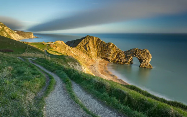 HD PC desktop wallpaper: Durdle Door, England — grassy coastal path along the horizon leading to a limestone sea arch over calm ocean.