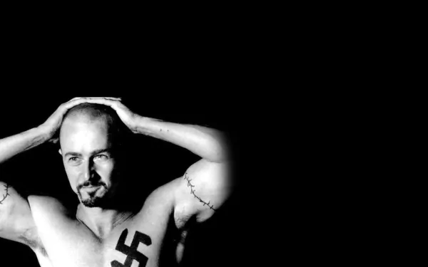 Black and white HD wallpaper featuring Ed Norton from the movie American History X, showing him shirtless with a prominent swastika tattoo on his chest against a stark black background.