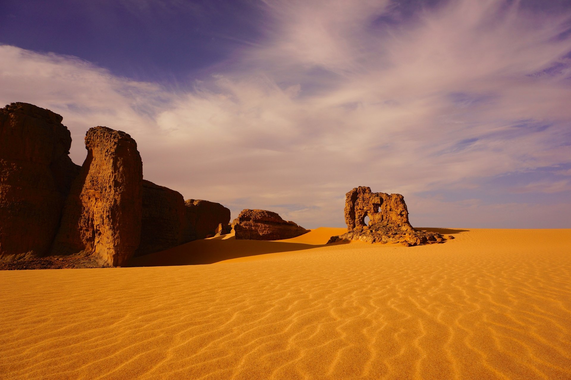 Vast Sahara desert landscape in Algeria with expansive golden sand dunes and rocky formations under a partly cloudy sky, captured in stunning 4K Ultra HD quality.