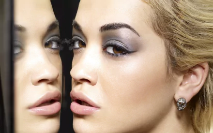 A close-up HD wallpaper of a singer with brown eyes gazing into a mirror, creating a reflection of her face. The singer is English and identified by the tag 'Rita Ora'.