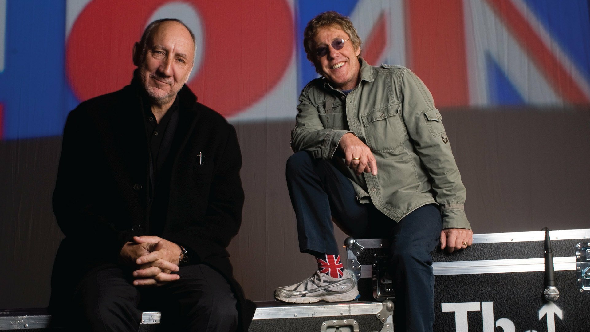 HD music PC wallpaper: two seated rock musicians on stage cases with a Union Jack backdrop — The Who–themed desktop background.