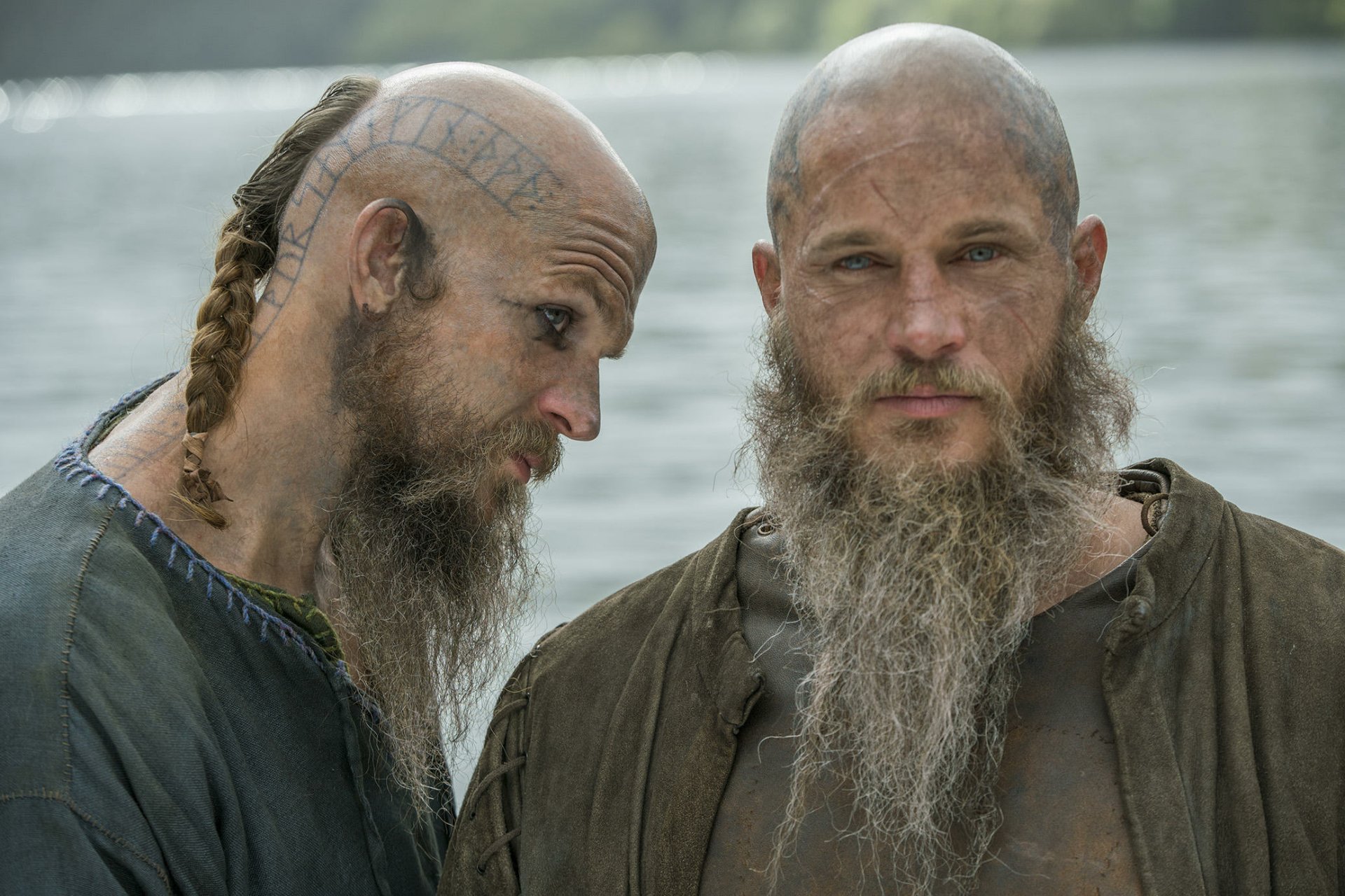HD PC desktop wallpaper from the TV show Vikings (2013) featuring two bearded men with shaved heads and braided hair by a riverside.