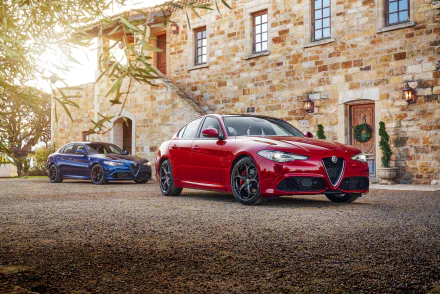 HD PC desktop wallpaper featuring two sleek Alfa Romeo cars parked in front of a rustic stone building bathed in warm sunlight.