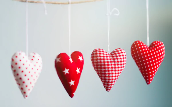 Four hanging fabric hearts in red and white patterns, representing love and romance, create a charming backdrop for Valentine's Day. This image serves as a vibrant 4K Ultra HD desktop wallpaper.