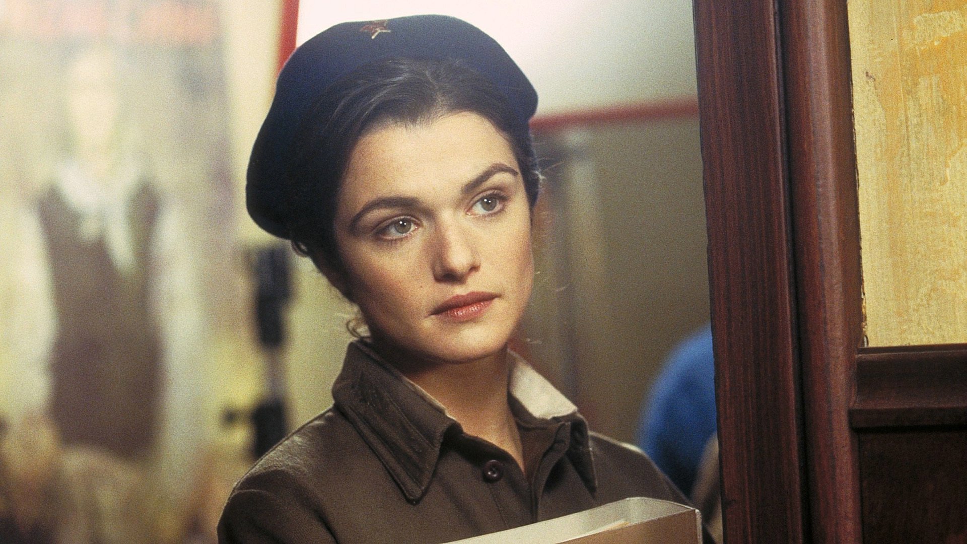 HD PC desktop wallpaper: scene from the movie Enemy At The Gates — close-up of a woman in wartime uniform and beret, holding papers, thoughtful expression in a dim corridor.