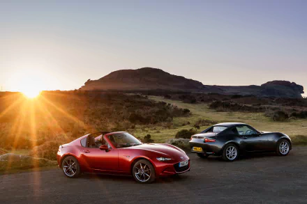 A red and a black Mazda MX-5 sports car parked on a scenic road at sunset, captured in sharp 4K Ultra HD quality for a PC desktop wallpaper.