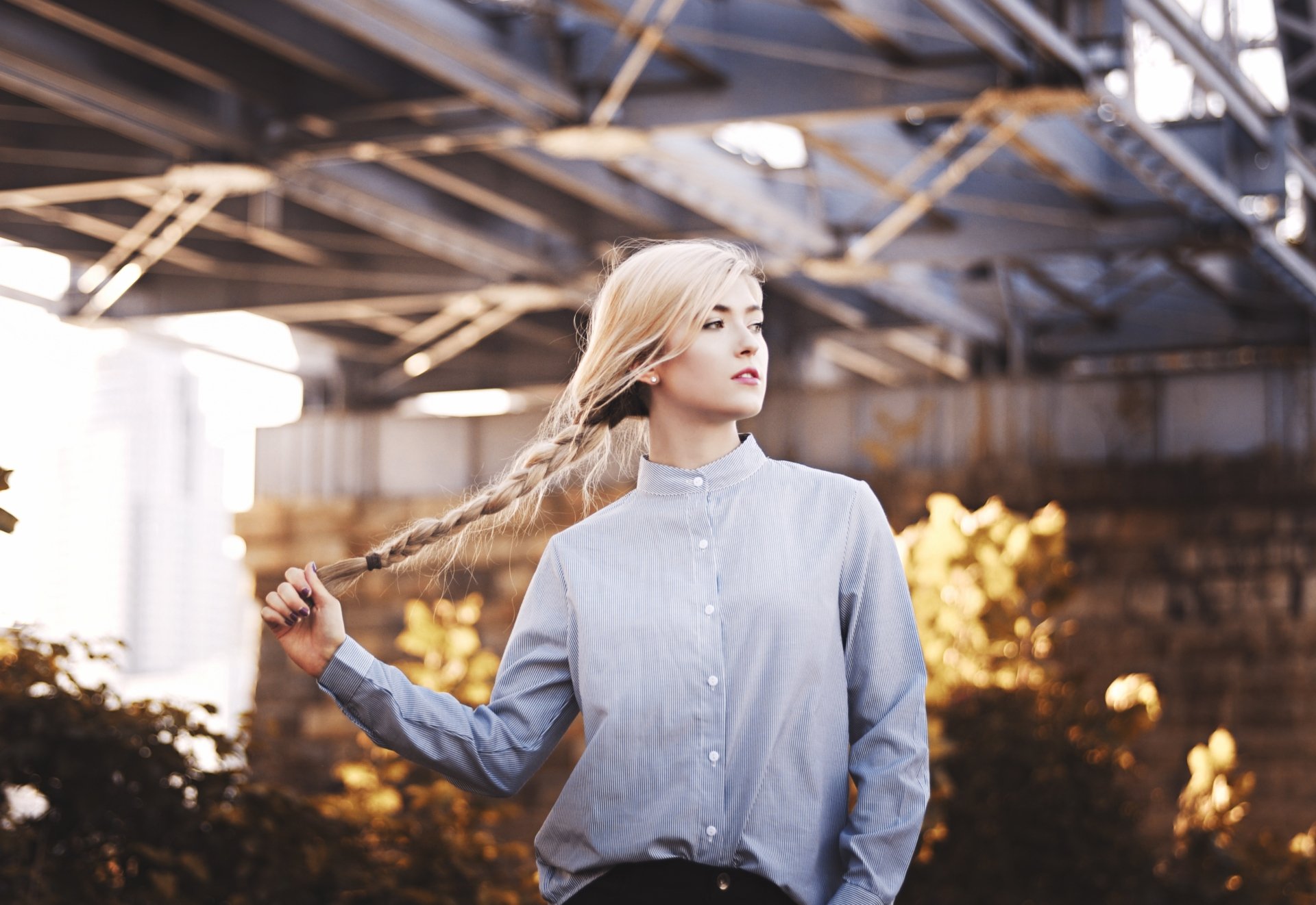 HD desktop wallpaper featuring a blonde woman model with a braided hairstyle, captured with a shallow depth of field under an industrial structure.
