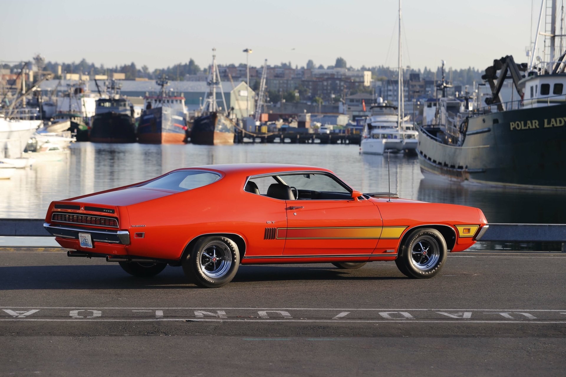 Orange Ford Torino Cobra/GT muscle car vehicle parked on a waterfront dock with boats, 5K Ultra HD PC desktop wallpaper background.