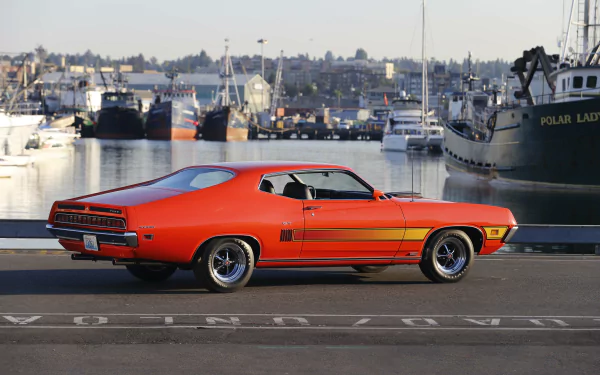 Orange Ford Torino Cobra/GT muscle car vehicle parked on a waterfront dock with boats, 5K Ultra HD PC desktop wallpaper background.