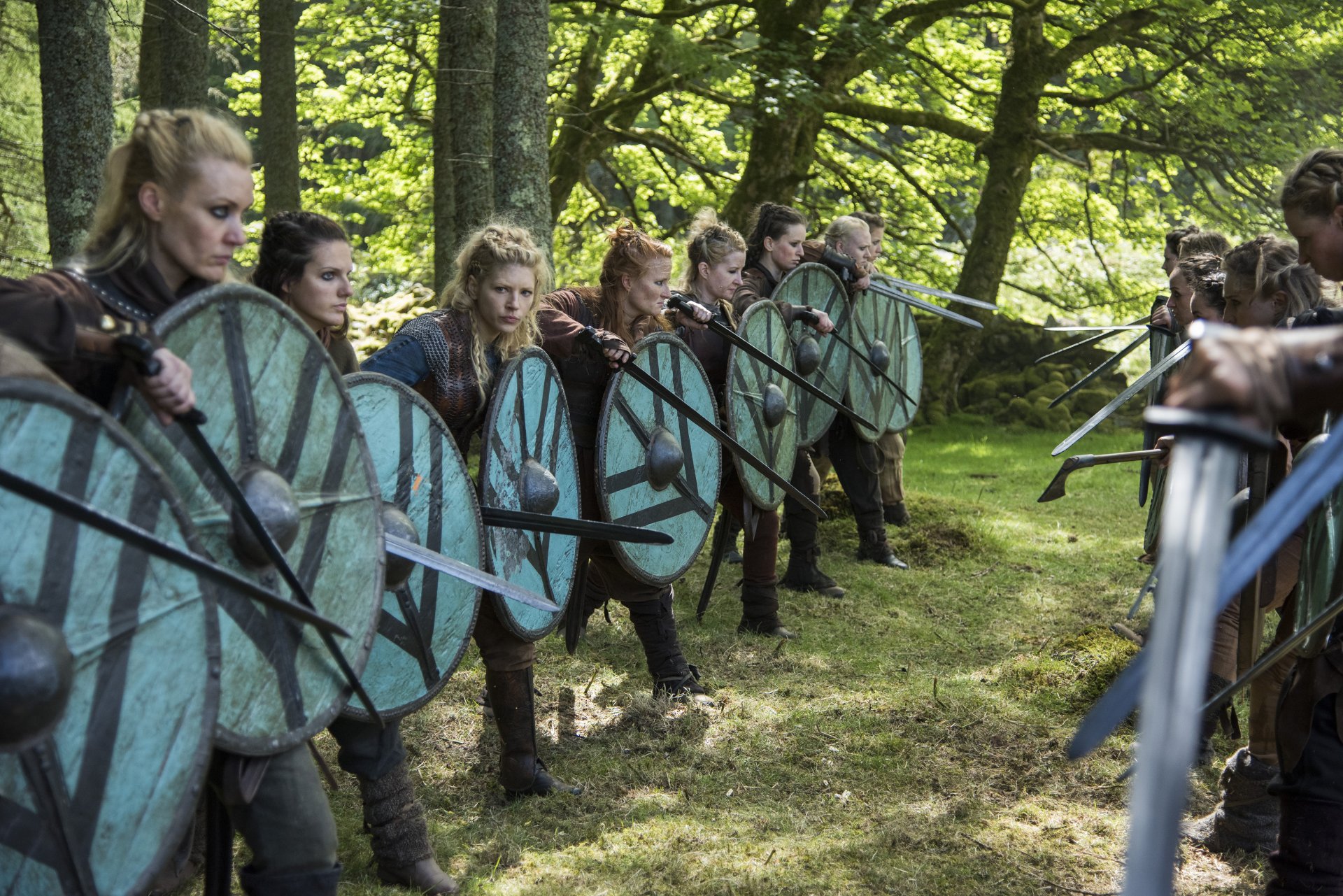 Scene from Vikings (2013) featuring Lagertha, played by Katheryn Winnick, with warriors lined up in a forest holding shields and swords in this HD PC desktop wallpaper.