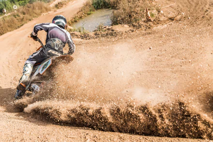 A motocross rider kicks up dirt as they speed around a bend on a dirt track, showcasing the thrill of the sport. HD wallpaper and background.