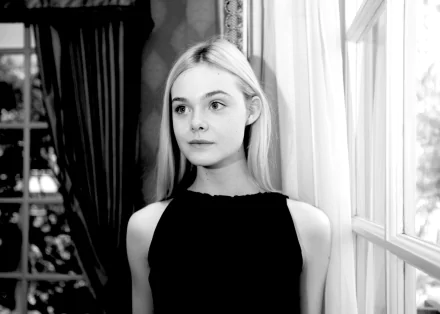 Black and white portrait of blonde American actress Elle Fanning, captured in a contemplative pose by a window, featured as an HD PC desktop wallpaper.