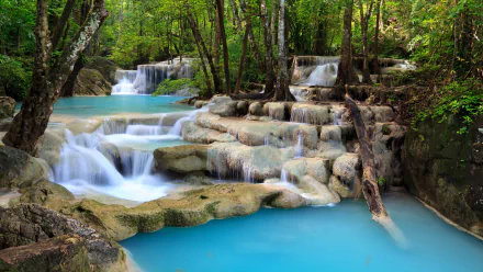 HD desktop wallpaper featuring a stunning waterfall in a forest, with turquoise waters cascading over rocks and lush greenery. Foamy water adds to the serene nature of the scene.
