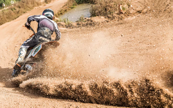A motocross rider kicks up dirt as they speed around a bend on a dirt track, showcasing the thrill of the sport. HD wallpaper and background.