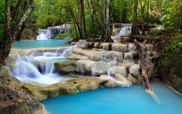 HD desktop wallpaper featuring a stunning waterfall in a forest, with turquoise waters cascading over rocks and lush greenery. Foamy water adds to the serene nature of the scene.