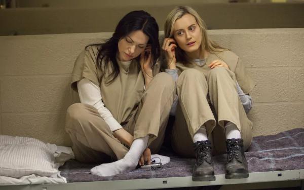Two women in prison uniforms sit closely together on a bed in a scene from the TV show Orange Is the New Black. HD desktop wallpaper and background.