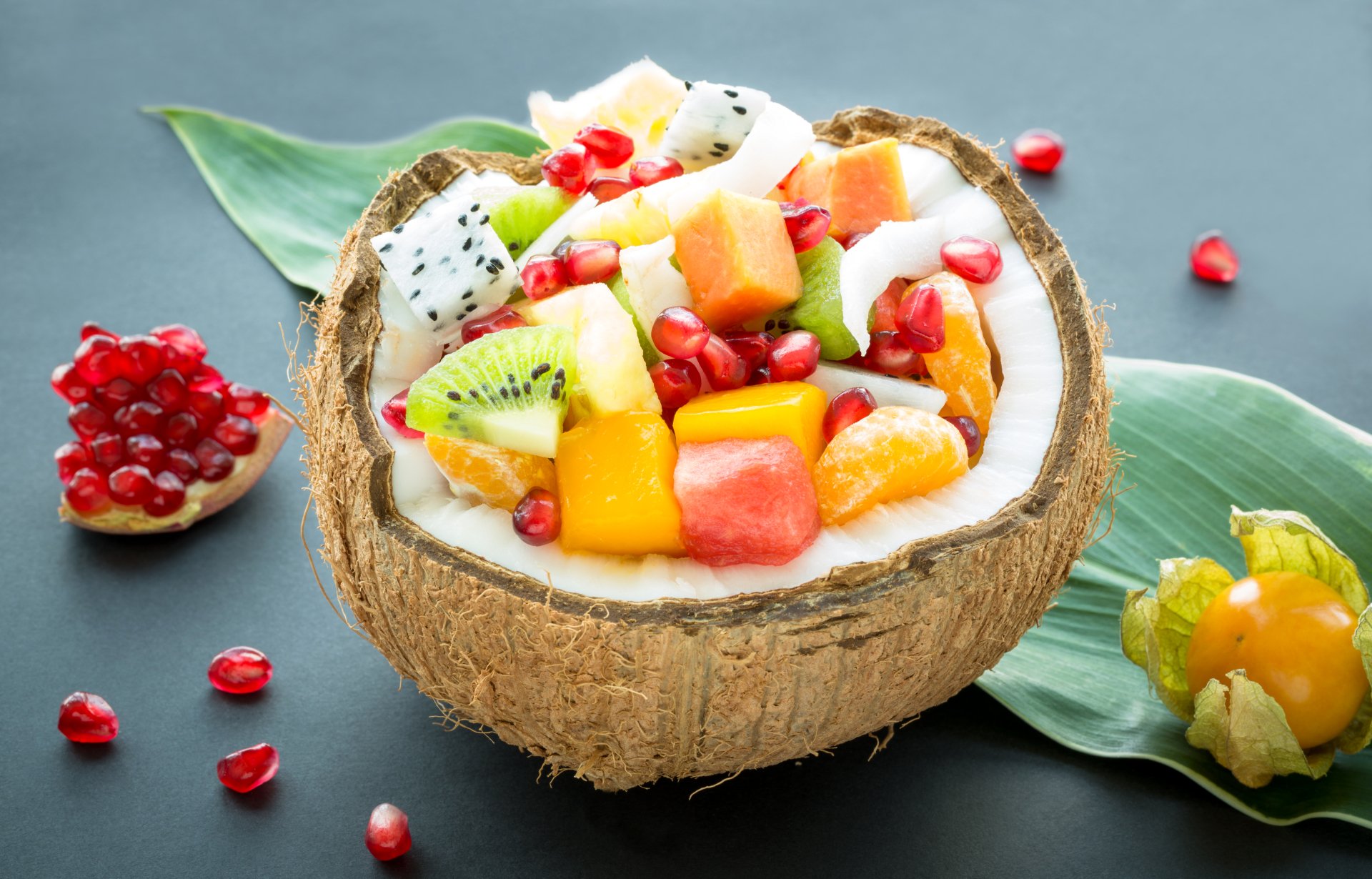 Colorful tropical fruit salad featuring coconut, kiwi, pomegranate, and other fruits, presented in a coconut shell on green leaves, captured in 4K Ultra HD quality.