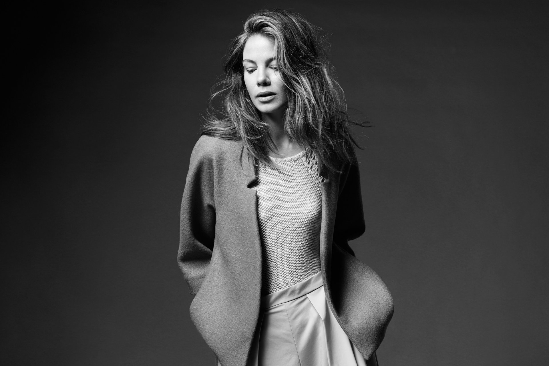 Black and white HD portrait of American actress Michelle Monaghan with tousled hair, wearing a blazer and skirt against a plain dark background.