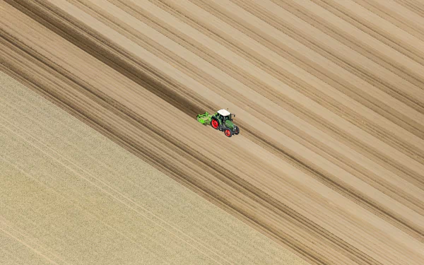 Aerial HD wallpaper of a tractor working in a patterned field, showcasing agricultural machinery and textured farmland from above.