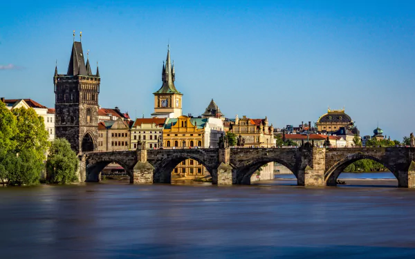 HD PC desktop wallpaper of Prague, Czech Republic: Charles Bridge spanning the Vltava with historic buildings and towers under a clear blue sky.