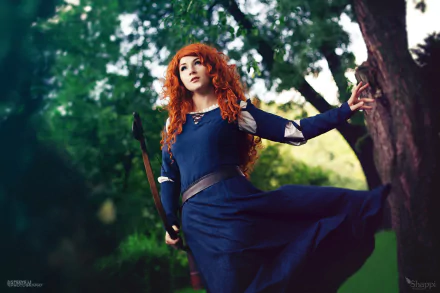 A woman cosplaying as Merida from Brave stands against a lush, green forest backdrop. She wears a blue dress and carries a bow, her red hair flowing in the natural light. The image features a subtle bokeh effect.
