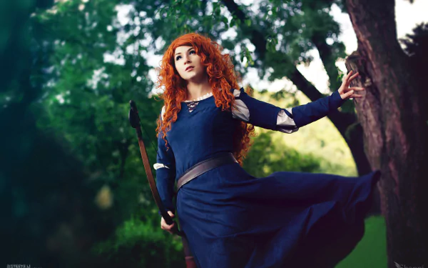 A woman cosplaying as Merida from Brave stands against a lush, green forest backdrop. She wears a blue dress and carries a bow, her red hair flowing in the natural light. The image features a subtle bokeh effect.