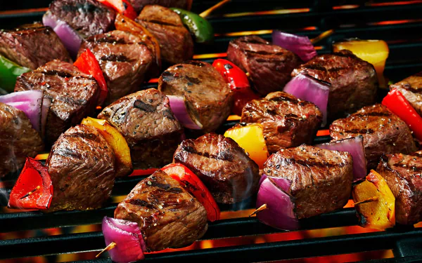 HD PC desktop wallpaper of grilled meat and colorful vegetables sizzling on a barbecue, showcasing juicy steaks, bell peppers, and red onions.