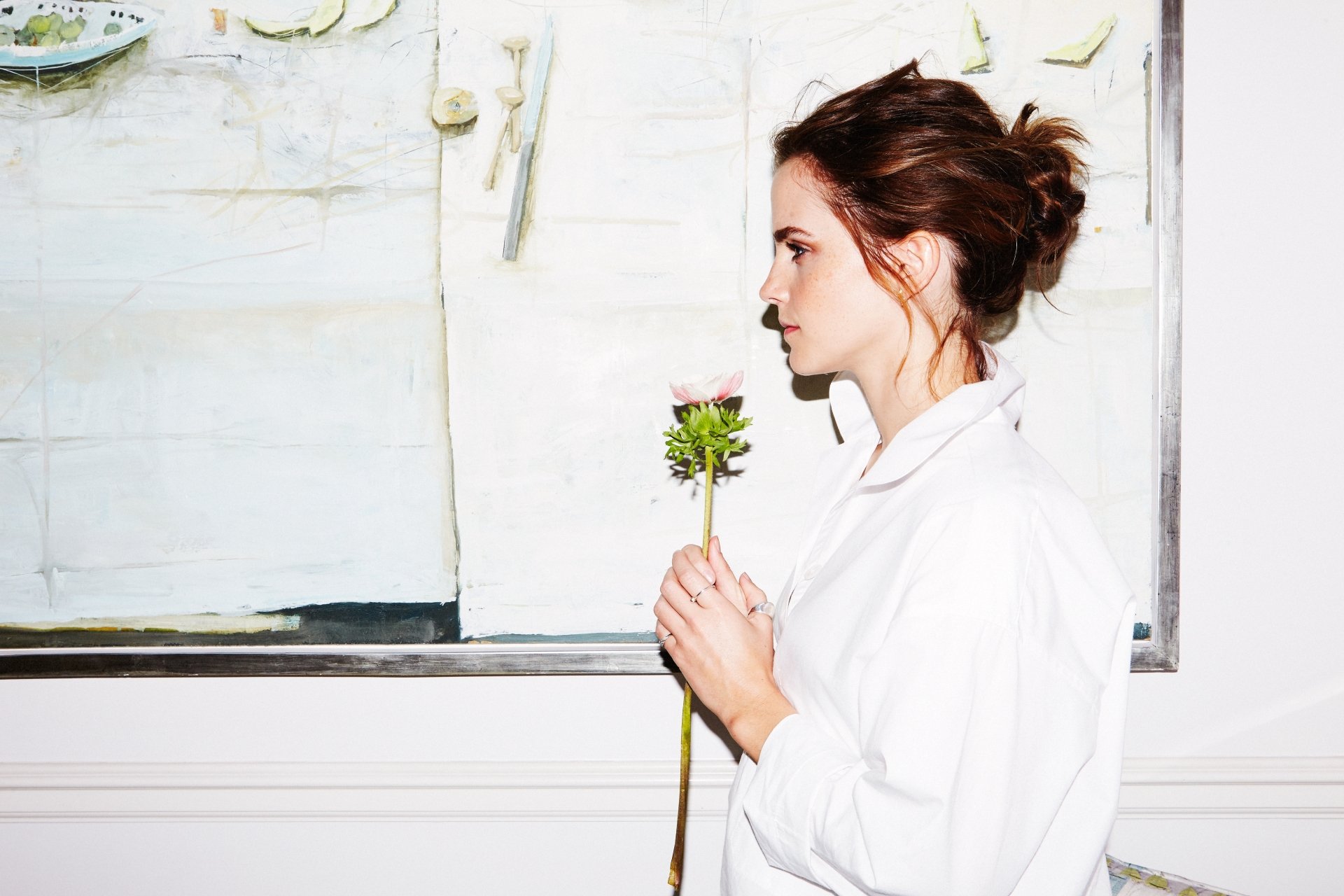 Profile of brunette English actress Emma Watson holding a single flower against a light, minimalist background in a 4K Ultra HD desktop wallpaper.