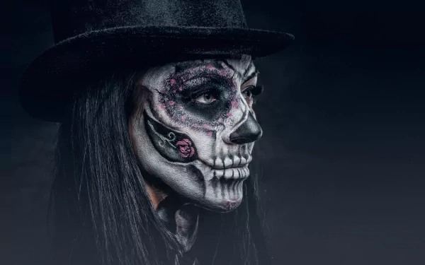 An artistic HD desktop wallpaper featuring a face with black hair and sugar skull makeup, showcasing intricate detailing, set against a dark background.