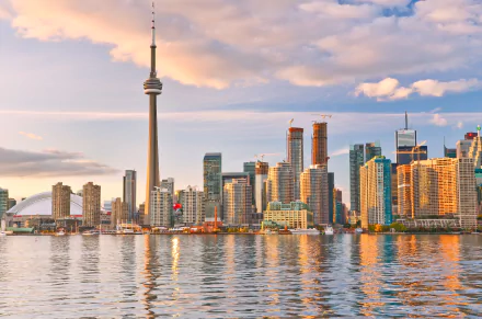 Toronto cityscape featuring towering skyscrapers and the iconic CN Tower at sunset, reflected in the waters. This HD wallpaper captures the vibrant atmosphere of this Canadian metropolis.