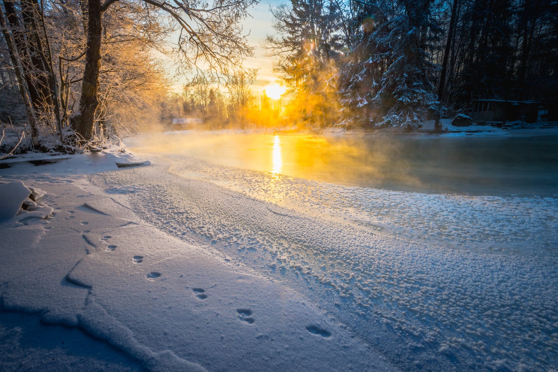 Winter sunrise over a snowy riverbank with footprints in the snow, captured in a 4K Ultra HD nature desktop wallpaper.