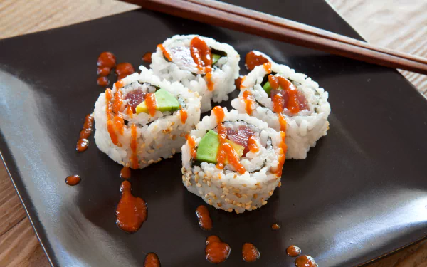 5K Ultra HD PC wallpaper: close-up sushi rolls of rice, fresh fish and avocado topped with spicy sauce on a black plate with chopsticks.