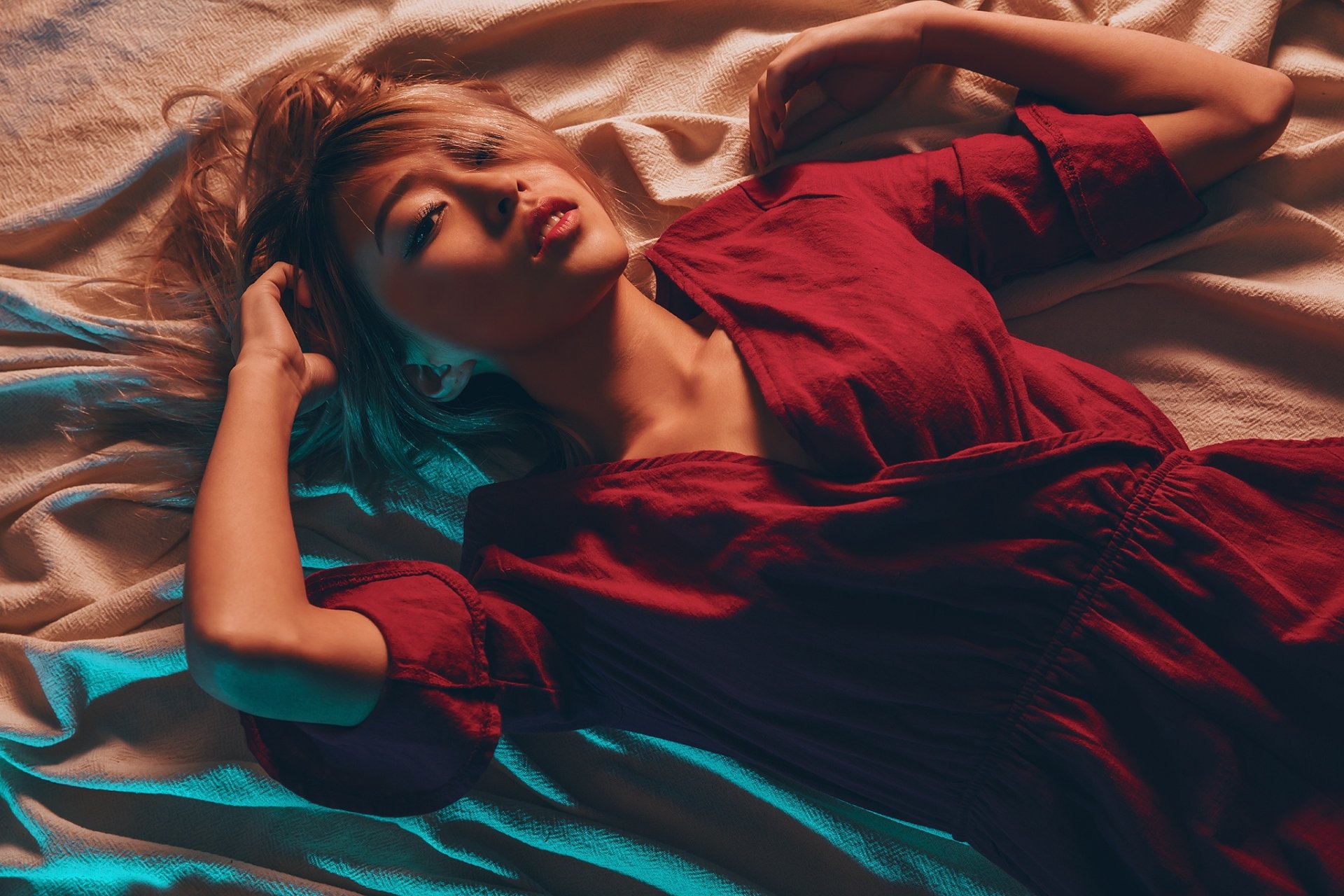 HD PC desktop wallpaper: woman model in a red dress lying on rumpled fabric, moody colored lighting and a relaxed, elegant pose.