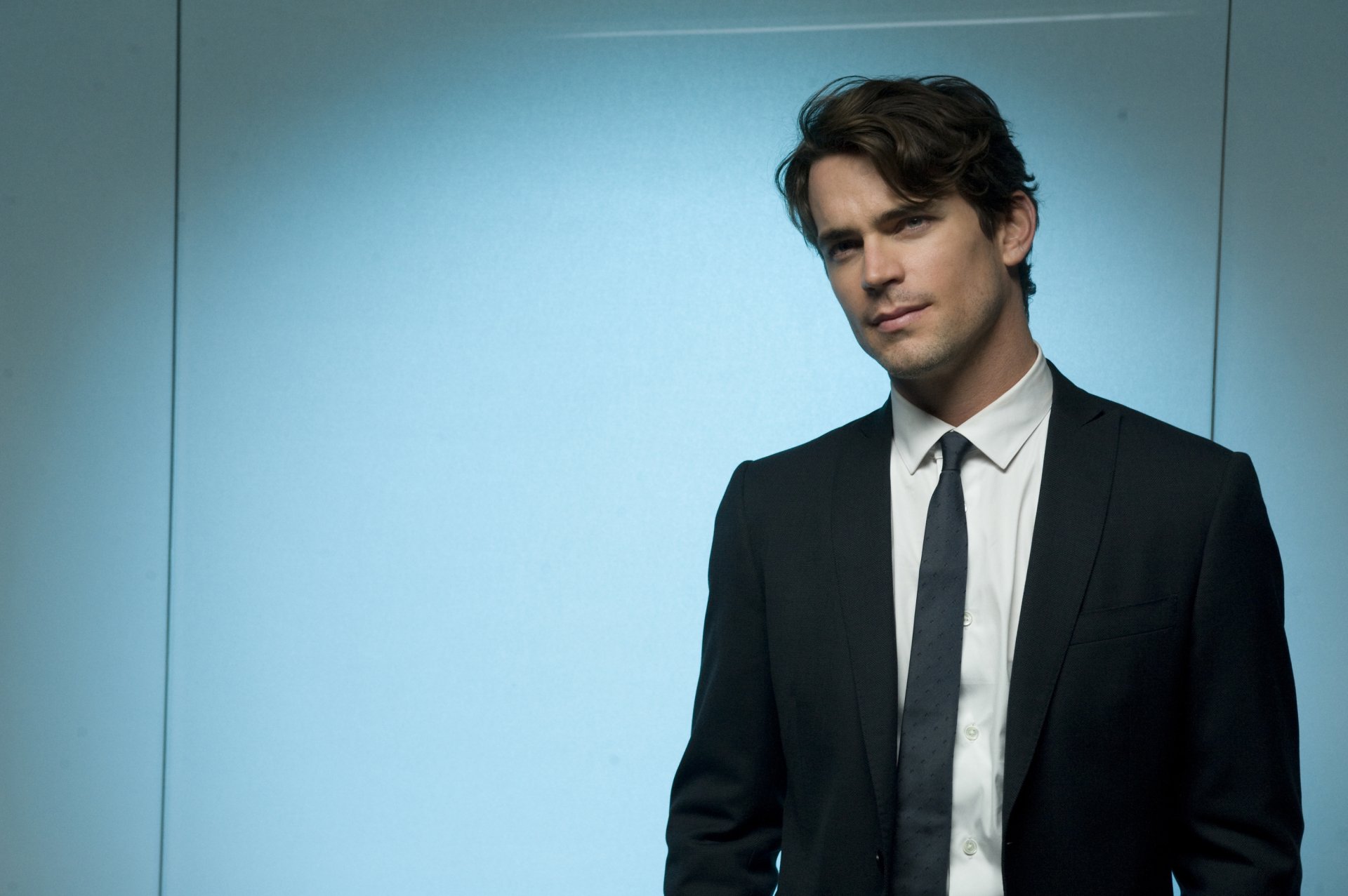 HD desktop wallpaper featuring a man in a black suit and tie with a light blue background.