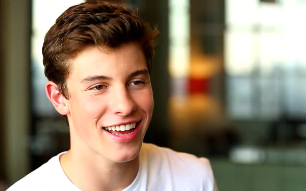 HD desktop wallpaper featuring a smiling person in a white shirt with a blurred background, tagged as Shawn Mendes.