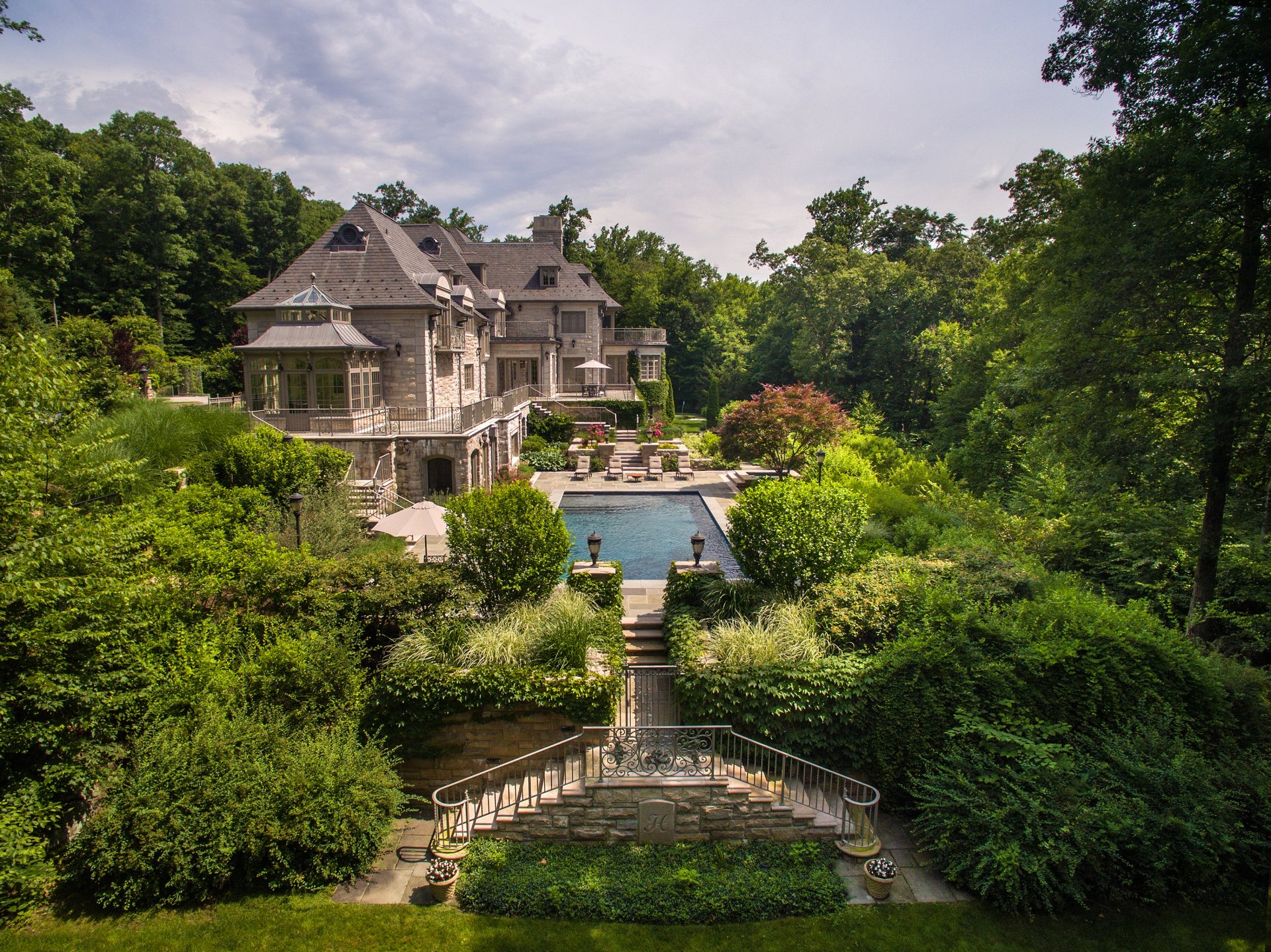 2K Quad HD PC desktop wallpaper/background of a luxurious man-made mansion and pool framed by terraces and lush gardens.