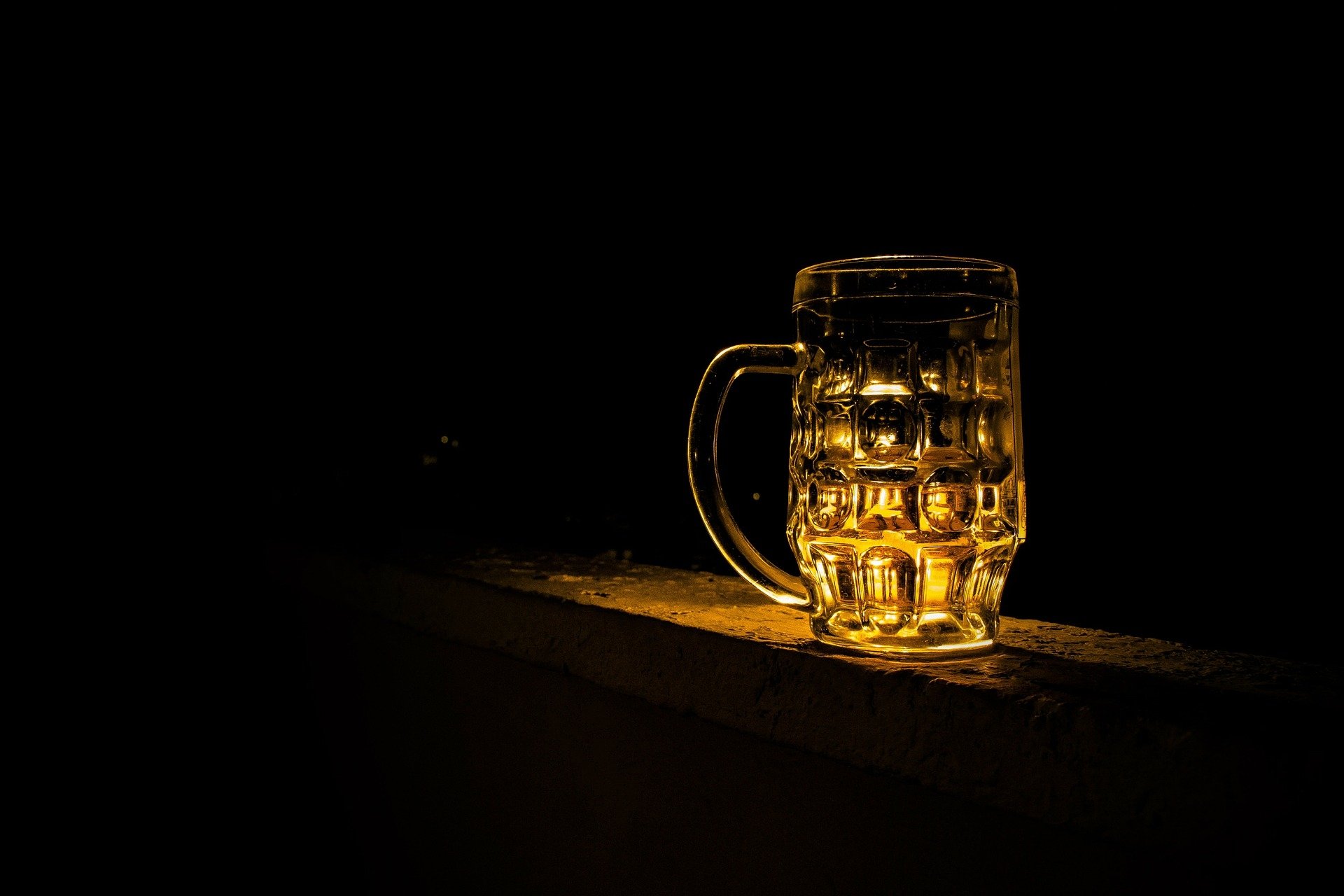 HD PC desktop wallpaper showing a glowing beer mug on a dark surface, highlighting the rich amber color and textured glass, evoking a cozy food and drink atmosphere.