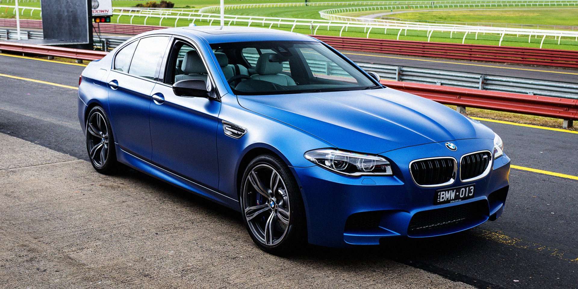 Blue BMW 5 Series sedan on a racetrack pit lane — high-resolution HD PC desktop wallpaper showcasing the BMW vehicle.