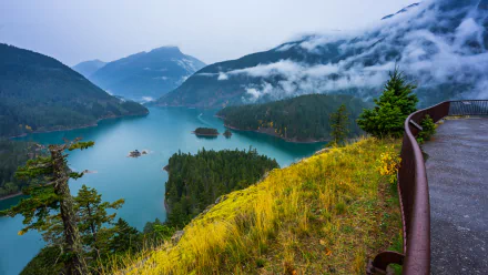 A vibrant HD desktop wallpaper showcasing Diablo Lake surrounded by lush forest and misty mountains under a cloudy sky.