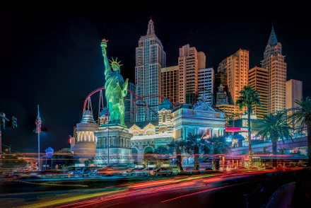 A vibrant time-lapse night view of Las Vegas featuring illuminated skyscrapers, the Statue of Liberty replica, and dynamic light trails in this HD cityscape wallpaper.