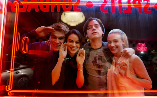 HD wallpaper featuring Riverdale cast members KJ Apa, Lili Reinhart, Cole Sprouse, and Camila Mendes, pictured together inside a neon-lit diner.