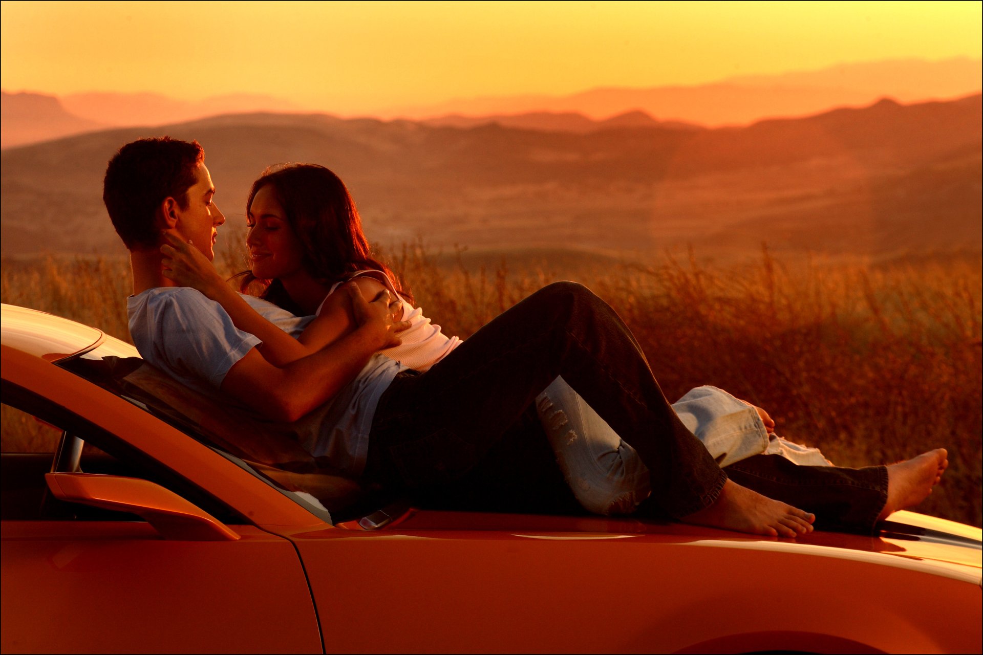 Megan Fox and Shia LaBeouf in a scene from the movie Transformers, embracing on the hood of a car at sunset. HD desktop wallpaper and background.